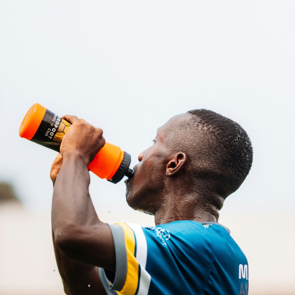 football with blue and yellow shirt on drinking water from an orange bottle