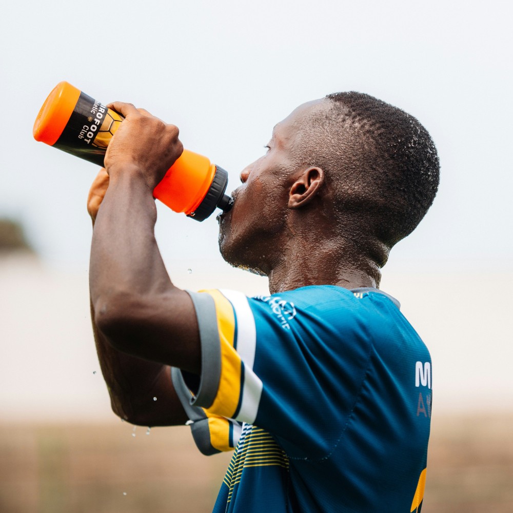 footballer with blue and yellow shirt on drinking water from an orange bottle