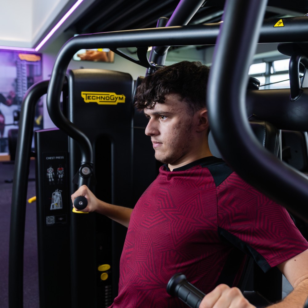 man using machine at the gym, wearing burgundy top