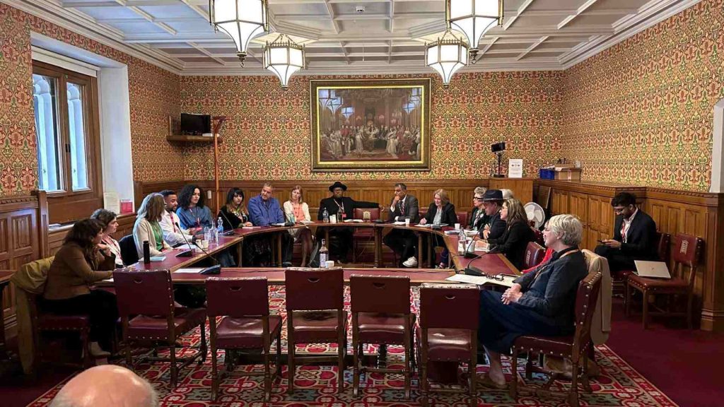 a room in the house of lords with 19 people sat around in a circle talking to each other.