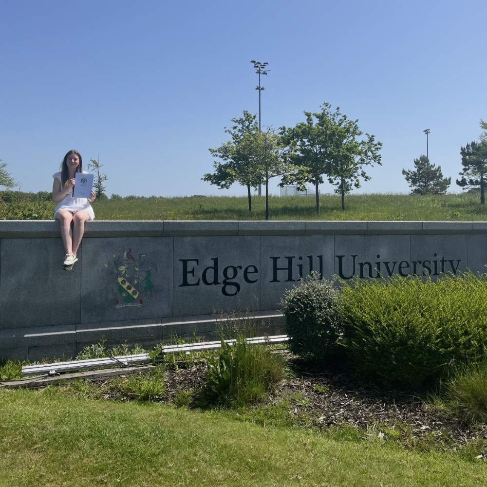 Student sitting on top of Edge Hill wall with logo on it.