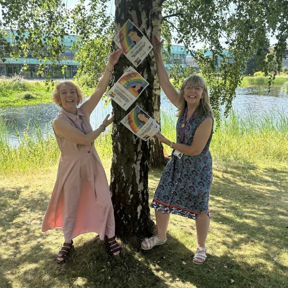 two women standing in front of a tree holding NHS posters up