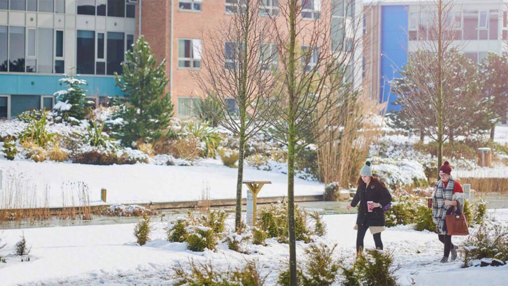 Students walking through our snowy campus. They are wearing wooly hats and winter coats.