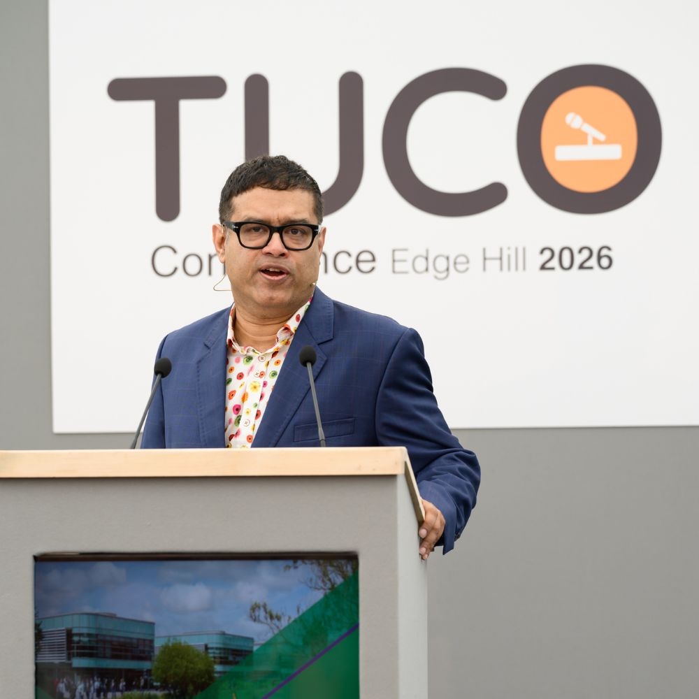 Someone on a poodium addressing the audience with bug sighn behind him saying TUCO conference at Edge Hill 2026