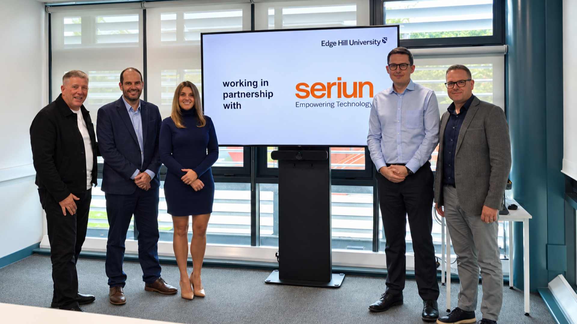 five people standing in front of a tv screen with edge hill logo and seriun.
