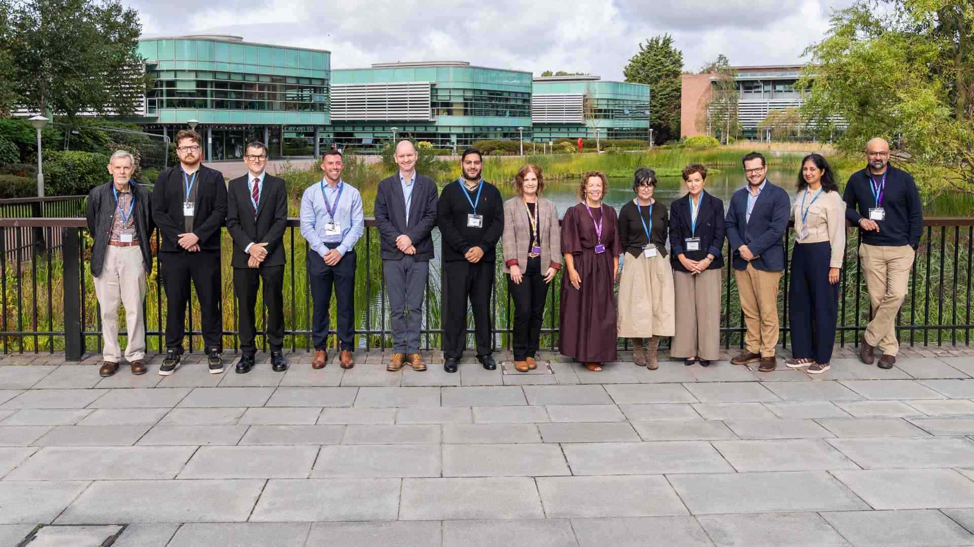 staff from edge hill standing behind lake o n Edge Hill campus smiling