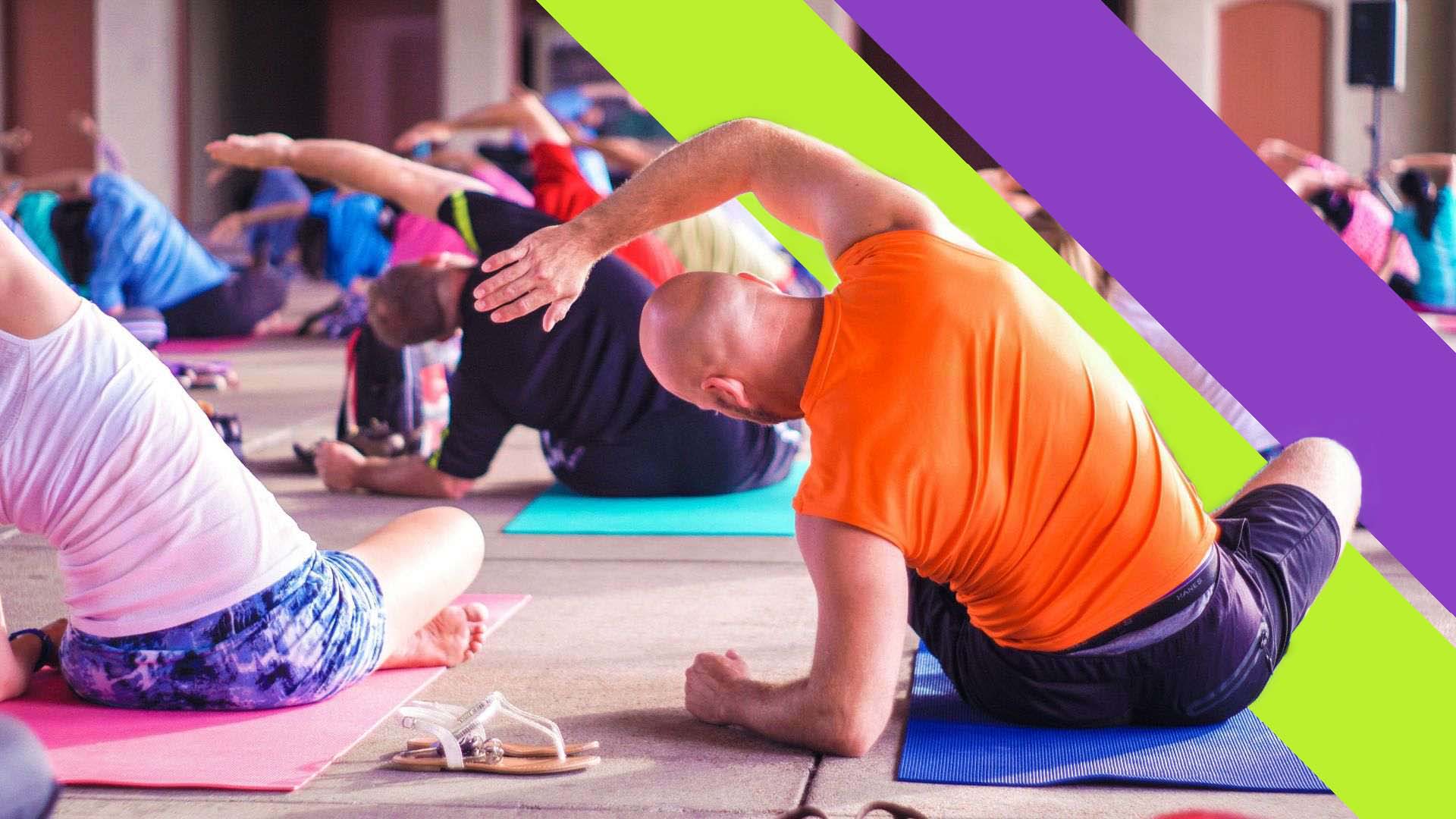 Several people in colourful gym wear sit on mats and stretch their right arms over their heads with the Edge Hill Sport double sash