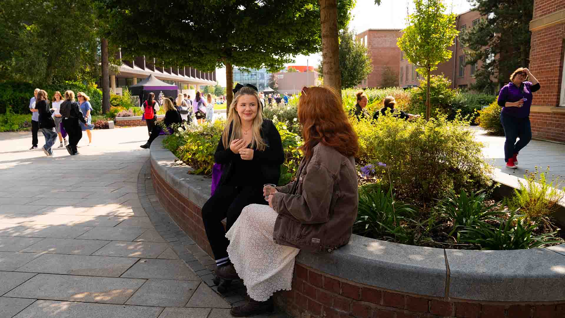 two female students sat on a wall near the hub during an open day