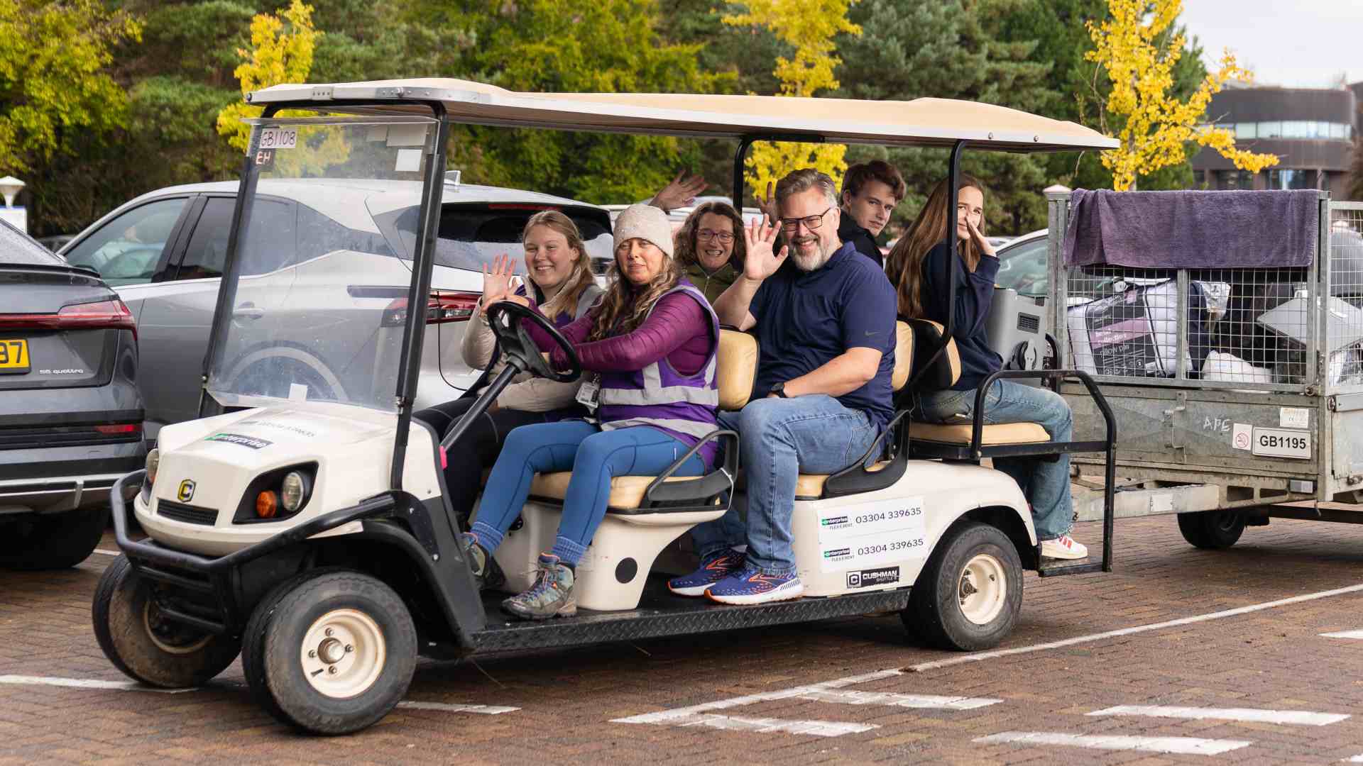 an electric buddy with 6 people on it waving to the camera.