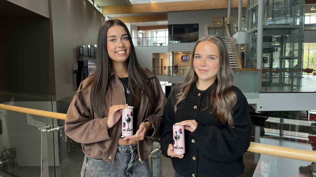 two students standing by glass balcony holding can designs