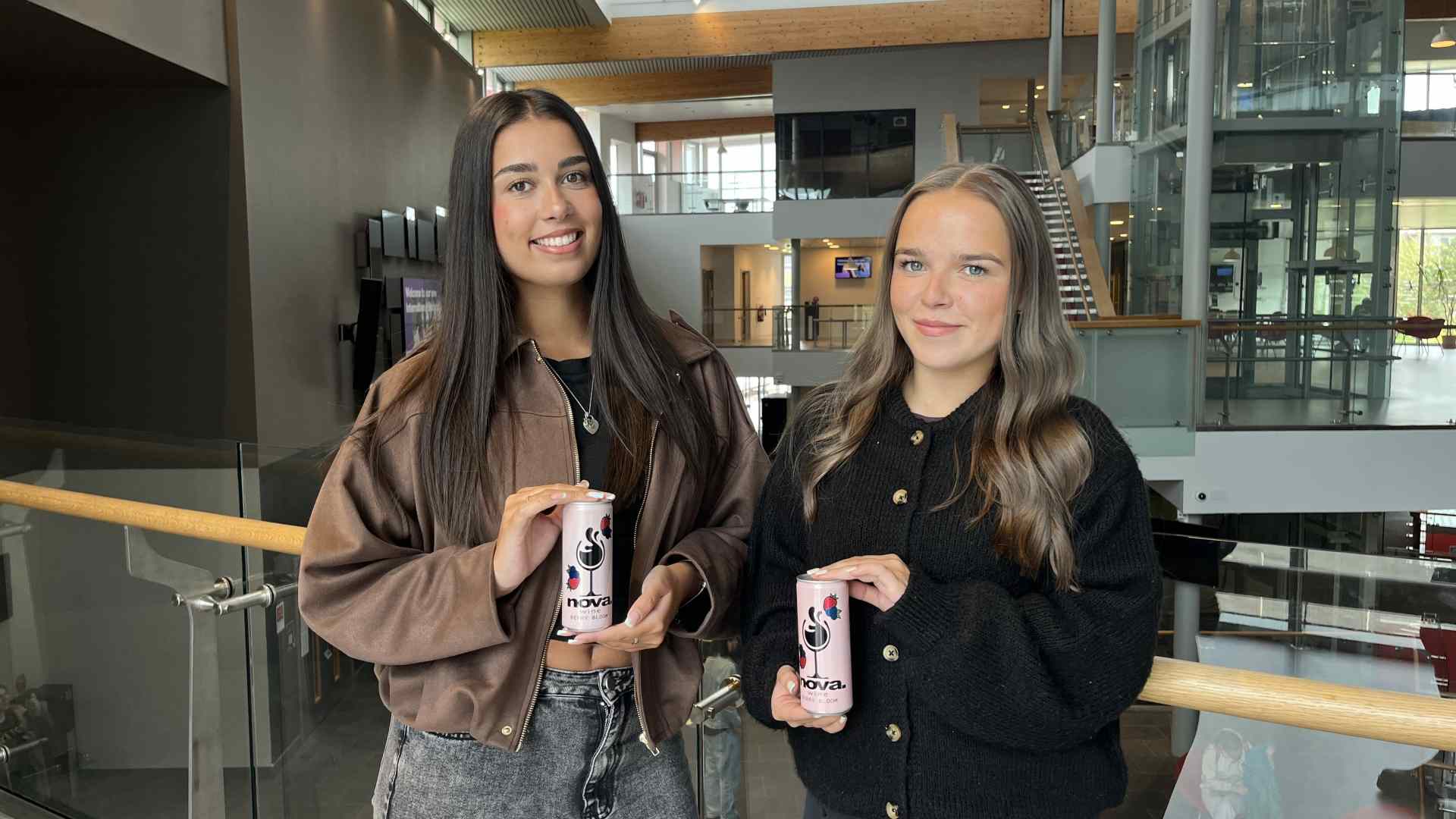 two students standing by glass balcony holding can designs
