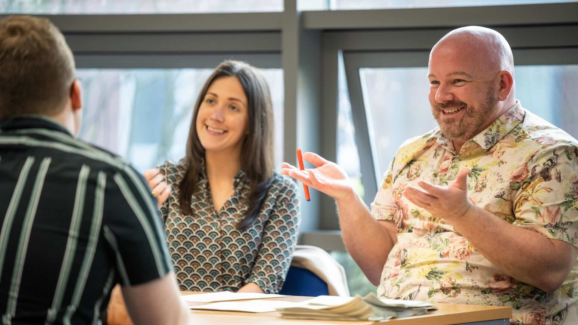 three people sitting on a table, talking and laughing